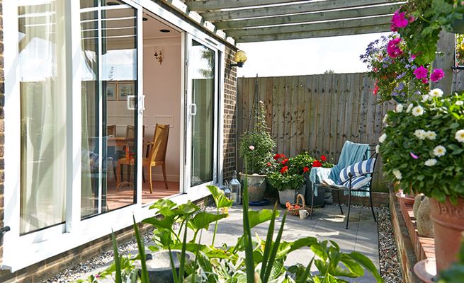 Aluminium sliding patio doors in white with white door handles with view of garden patio with wooden pergola