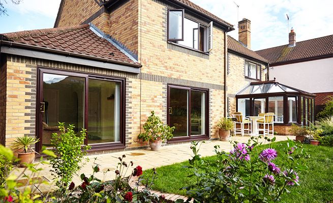 Dark woodgrain uPVC patio doors with gold handles and Victorian conservatory garden patio view