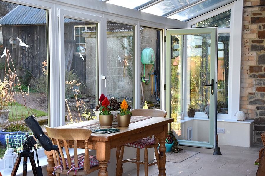 Dual sage green L shaped conservatory with uPVC French doors in open position
