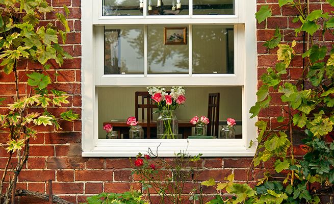 White double glazed timber sash window with cottage bars in with roses on windowsill from Anglian Home Improvements