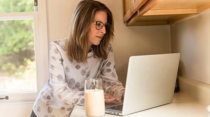 Woman contacts Anglian Home Improvements for a quote from on her laptop in the kitchen